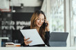 © Phushutter - Portrait of executive Asian financial woman sitting at desk and working on tablet while making call.