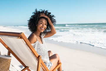 happy smiling young woman sitting on deck chair at beach during summer vacation