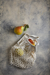 Wall Mural - pears in a knitted white bag on gray with navy cement background, ceramic. place for text.