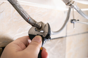 plumber hand fixes flexible hoses by adjustable wrench closeup at home