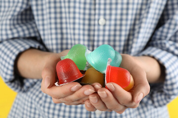 Woman holding many tasty bright jelly cups on yellow background, closeup