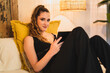 Chica joven delgada con pelo largo mirando tablet sobre la cama de un hotel estilo soho