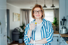 Healthy Habit To Drink Water. Smiling Middle Age Woman With Glass Of Pure Water With Lemon Standing On Her Kitchen. Control Body Hydration, Track Water Balance. Healthy Living. Selectivbe Focus.