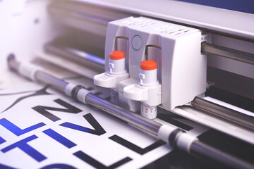 Leinwandbilder - cutting plotter machine with adjustable blades makes adhesive lettering from black vinyl foil in bright light with blue highlights. selective focus. advertising concept