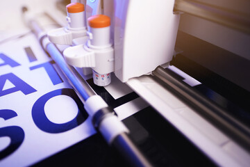 Leinwandbilder - tool head of cutting plotter with adjustable blades. making of adhesive lettering from black vinyl foil in bright light. side view with energetic blue light. selective focus. advertising concept