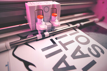Leinwandbilder - cutting plotter equiped with two adjustable blades makes adhesive lettering from black vinyl foil in energetic pink light. selective focus. advertising and political movement concept