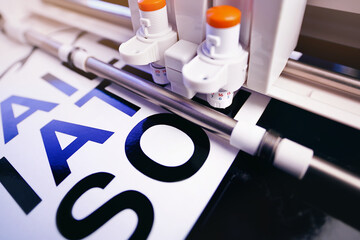 tool head of cutting plotter equiped with two adjustable blades makes adhesive lettering from black vinyl foil in bright light. selective focus. advertising concept