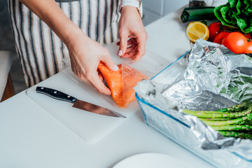 Wall Mural - Baked salmon with green asparagus recipe steps. Step one. Woman planning to slice fresh salmon on cutting board. Step by step recipe. Healthy cooking at home in the kitchen according to recipe.