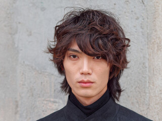 Portrait of handsome Chinese young man in black looking at camera with gray wall background, front view of confident young man, close up view head shot.