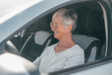 Wall Mural - Happy owner. Handsome mature woman sitting relaxed in his newly bought car looking at the road smiling joyfully. One old senior driving and having fun..