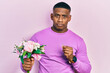 Young black man holding bouquet of flowers and wedding ring relaxed with serious expression on face. simple and natural looking at the camera.