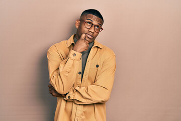 Wall Mural - Young black man wearing casual clothes and glasses serious face thinking about question with hand on chin, thoughtful about confusing idea