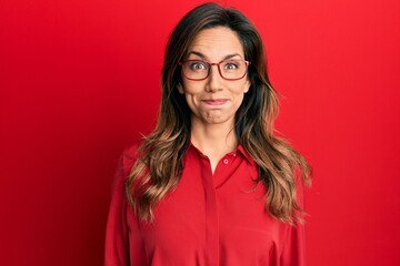 Poster - Young latin woman wearing casual clothes and glasses puffing cheeks with funny face. mouth inflated with air, crazy expression.