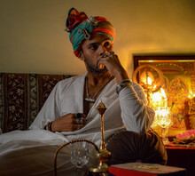 Indian Man Sitting Beside Hookah And Hindu Deity Icon With Lit Diya