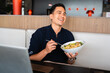 © Pintau Studio - Portrait of happy young handsome man laughing while eating a salad. Male sitting at table in lunch break from work.