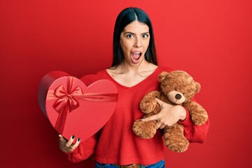 Wall Mural - Young hispanic woman holding valentine gift afraid and shocked with surprise and amazed expression, fear and excited face.