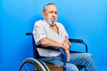 Wall Mural - Handsome senior man with beard sitting on wheelchair puffing cheeks with funny face. mouth inflated with air, crazy expression.