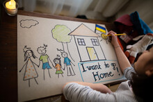 Top View Of Ukrainian Refugee Schoolgirl Missing Home And Drawing Her Family. Ukrainian War Concept.