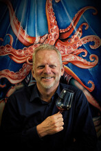 Smiling Middle Aged Man Holding A Glass Of Red Wine Against Background With Octopus Graphic