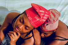 Two Young African Women With Red Kufi Hats Posing Against Light Textile Outdoor