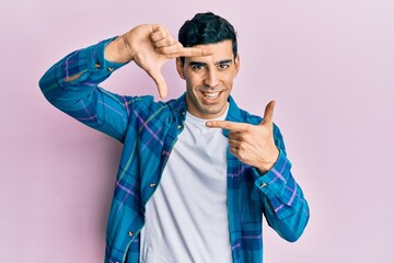 Wall Mural - Handsome hispanic man wearing casual clothes smiling making frame with hands and fingers with happy face. creativity and photography concept.
