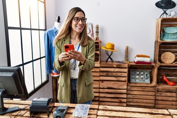 Young hispanic woman using smartphone working at clothing store