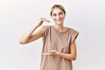 Sticker - Young blonde woman standing over isolated background gesturing with hands showing big and large size sign, measure symbol. smiling looking at the camera. measuring concept.