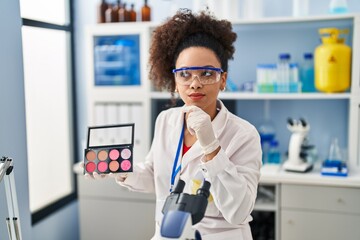 Wall Mural - Young african american woman working at scientist laboratory doing make up serious face thinking about question with hand on chin, thoughtful about confusing idea