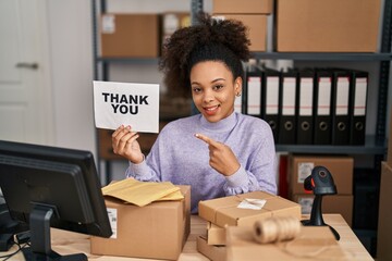 Wall Mural - Young african american woman working at small business ecommerce holding thank you banner smiling happy pointing with hand and finger