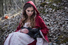Young Blonde Woman In Red Cloak Holding Dark Wolf