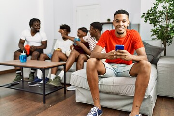 Poster - Group of african american people sitting on the sofa at home. Man smiling happy using smartphone.