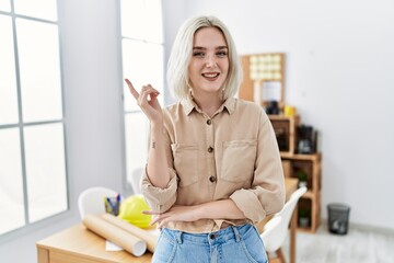 Sticker - Young beautiful caucasian woman at construction office with a big smile on face, pointing with hand and finger to the side looking at the camera.