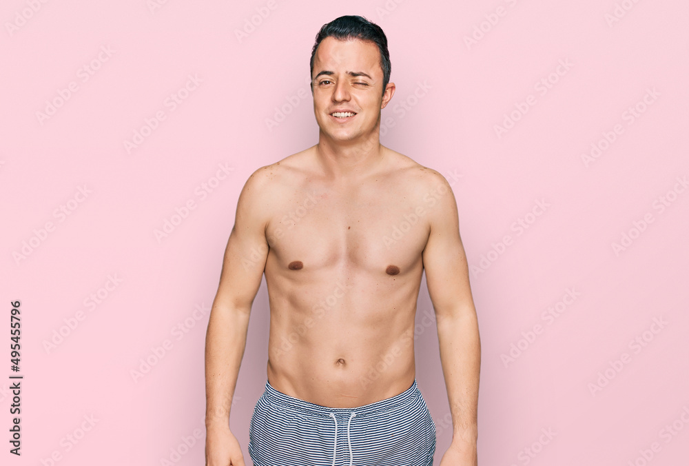 Handsome young man wearing swimwear shirtless winking looking at the camera with sexy expression, cheerful and happy face.