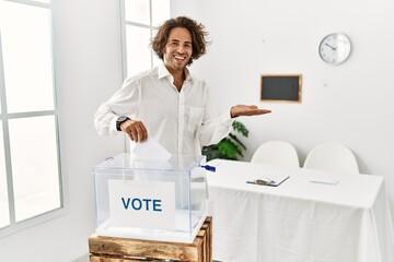 Sticker - Young hispanic man voting putting envelop in ballot box pointing aside with hands open palms showing copy space, presenting advertisement smiling excited happy