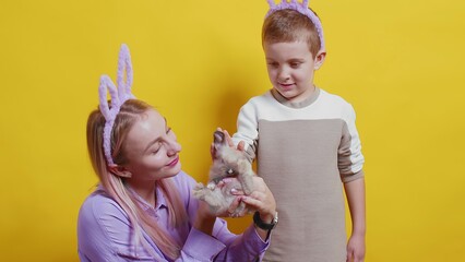 A girl and a boy with bunny ears on a yellow background. A girl is holding a rabbit. Easter