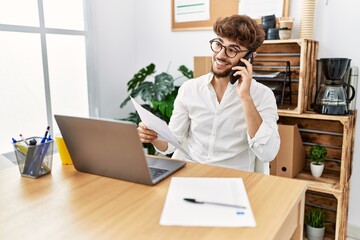 Wall Mural - Young arab man talking on the smartphone reading document at office