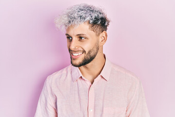 Wall Mural - Young hispanic man with modern dyed hair wearing casual pink shirt looking to side, relax profile pose with natural face and confident smile.