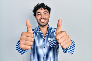 Sticker - Young hispanic man wearing casual clothes approving doing positive gesture with hand, thumbs up smiling and happy for success. winner gesture.