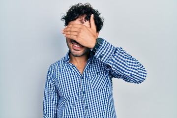 Poster - Young hispanic man wearing casual clothes smiling and laughing with hand on face covering eyes for surprise. blind concept.