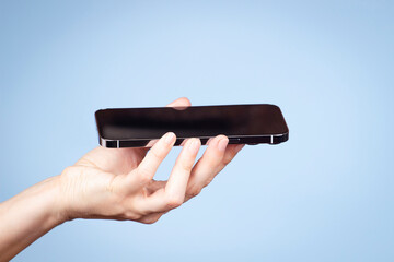 Woman hand holding smartphone screen face up side view on light blue background