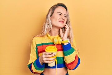 Poster - Beautiful young blonde woman drinking cup of coffee wearing headphones touching mouth with hand with painful expression because of toothache or dental illness on teeth. dentist concept.