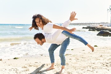 Poster - Middle age hispanic man smiling happy holding woman on his back at the beach.