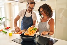 Middle Age Hispanic Couple Smiling Confident Pouring Food On Frying Pan At Kitchen