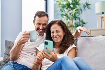 Canvas Print - Middle age man and woman couple using smartphone and drinking coffee at home