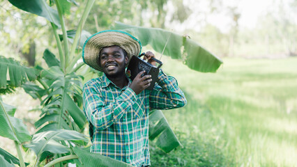 African farmer man listens retro radio broadcast receiver on shoulder stands happy smiling in his organic farm