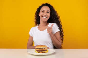 Wall Mural - Cheerful Lady Holding Burger Showing Thumb Up