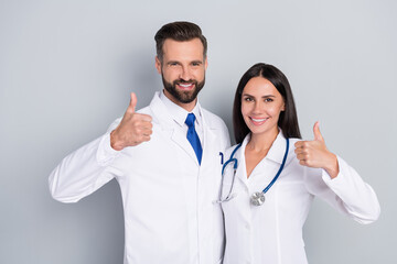 Canvas Print - Photo of smart happy two docs dressed white coats embracing showing thumbs up isolated grey color background