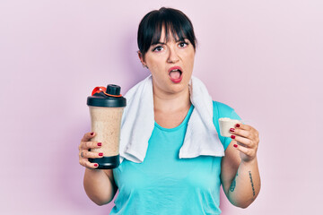 Canvas Print - Young hispanic woman wearing sportswear holding water bottle in shock face, looking skeptical and sarcastic, surprised with open mouth