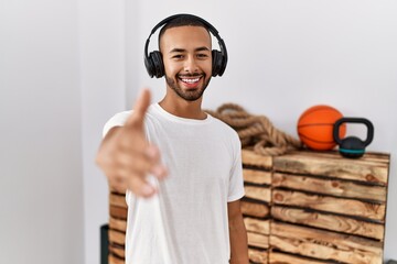 Poster - African american man listening to music using headphones at the gym smiling friendly offering handshake as greeting and welcoming. successful business.