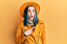 Young Modern Girl Wearing Yellow Hat And Leather Jacket Surprised Pointing With Finger To The Side, Open Mouth Amazed Expression.